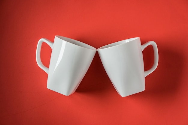 Top view of two white ceramic coffee cups in a red