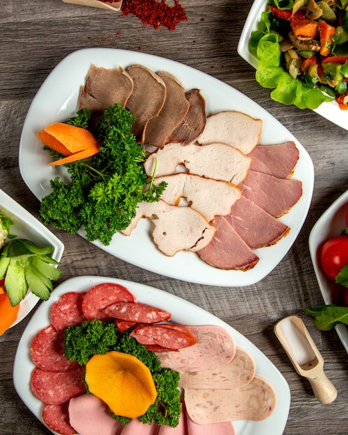 Top view a type of meat cuts on a plate with greens and sausage on the table