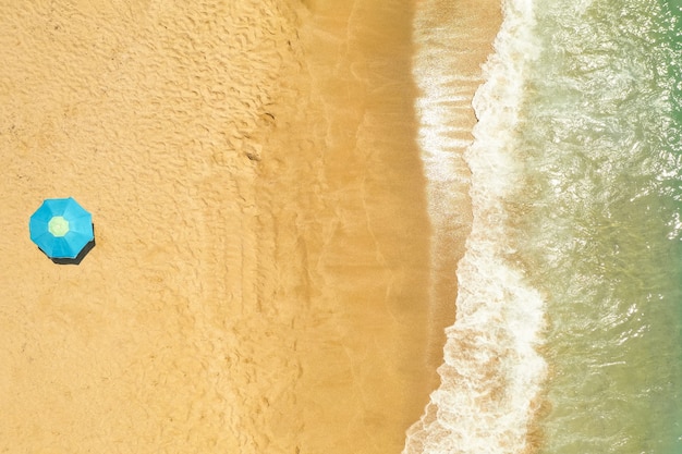 Vista dall'alto di ombrellone sulla spiaggia di sabbia dorata bagnata dalle onde del mar mediterraneo