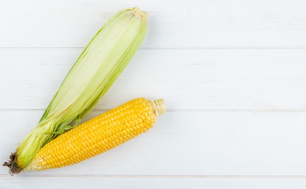 Top view of uncooked and cooked corns on left side and wooden surface with copy space