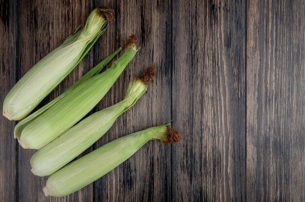 Top view of uncooked corns on left side and wooden surface with copy space