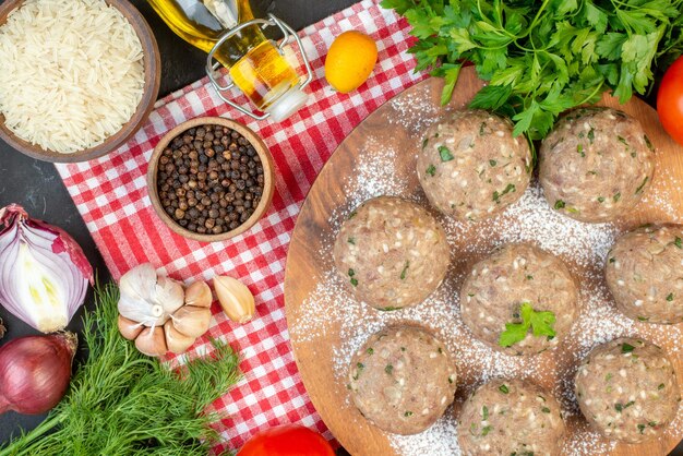 Top view of uncooked meat balls with green in a brown plate and rice fresh green lemon fallen oil bottle pepper on red stripped towel on black background