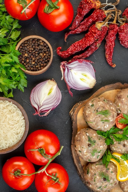 Top view of uncooked meatballs on a wooden cutting board and fresh vegetables green on dark background