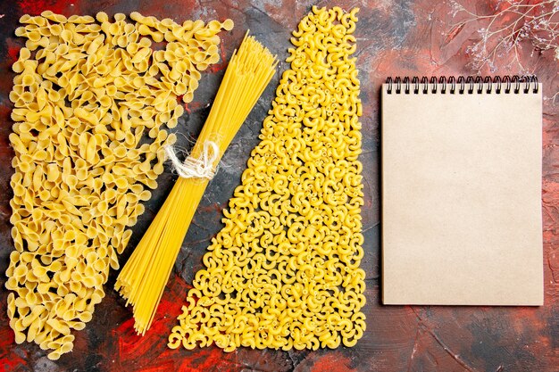 Top view of uncooked pasta as a form of spaggetti manicotti and notebook on black background