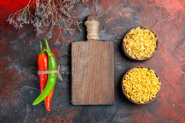 Foto gratuita vista dall'alto di pasta cruda peperoni di cayenna in diversi colori e dimensioni legati l'uno nell'altro con corda e tagliere di legno su sfondo di colore misto