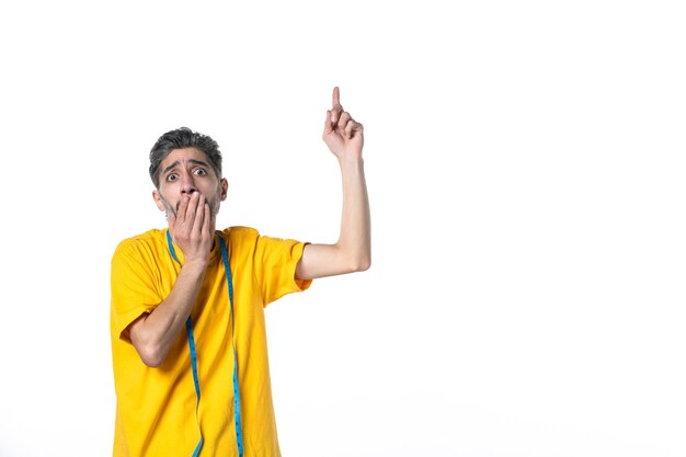 Top view of unhappy young guy in yellow shirt holding meter and pointing up on white surface