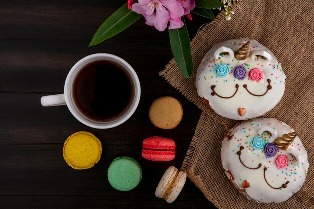 Top view unicorns with sweet donuts with a cup of tea and colored macaroons on a wooden table