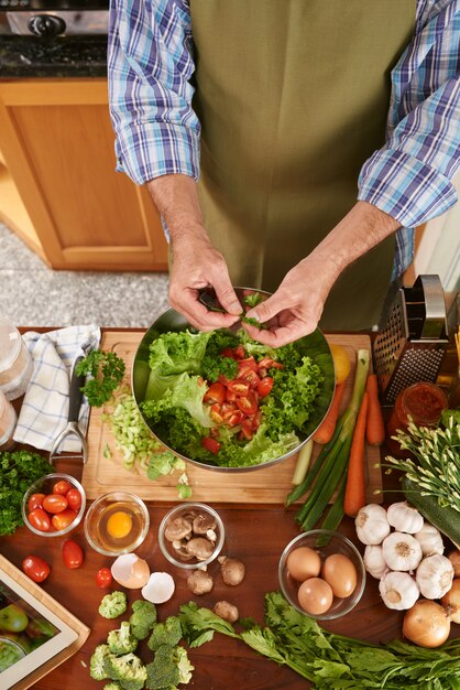 Top view of unrecognizable cook adding parsley to the salad bowl