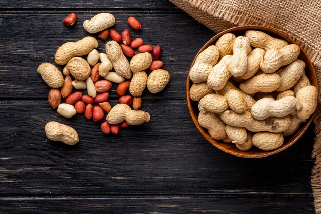 top view unshelled peanuts in a bowl with peeled on a black wooden table