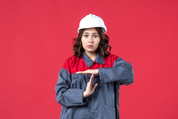 Top view of upset female builder in uniform with hard hat and making stop gesture on isolated red background