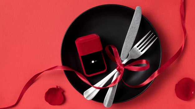 Top view of valentine's day engagement ring on plate with cutlery and ribbon
