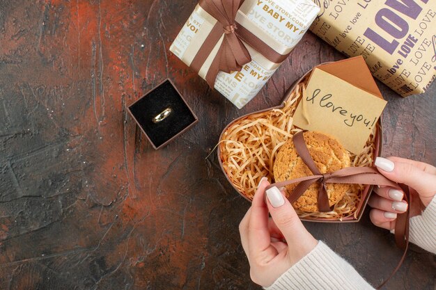 Вид сверху подарки на день святого валентина с кольцом и печеньем на темно-коричневом фоне любовь пара цвет подарок чувства брак праздник