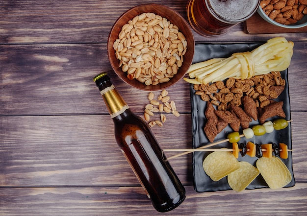 Top view of varied beer snacks with a bottle of beer on rustic with copy space