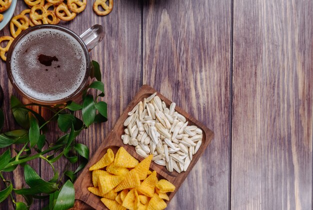 Top view of varied beer snackssunflower seeds chips and mini pretzels with a mug of beer on rustic with copy space