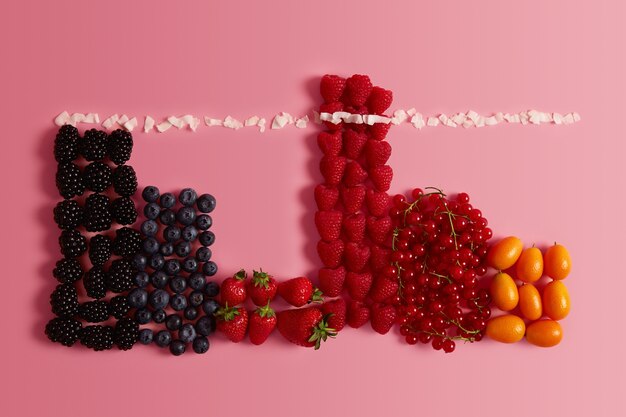 Top view of variety ripe delicious summer fruits. Healthy fresh berries. Blueberry, blackberry, strawberry, redcurrant and cumquat on pink background. Organic food, dieting and nutrition concept