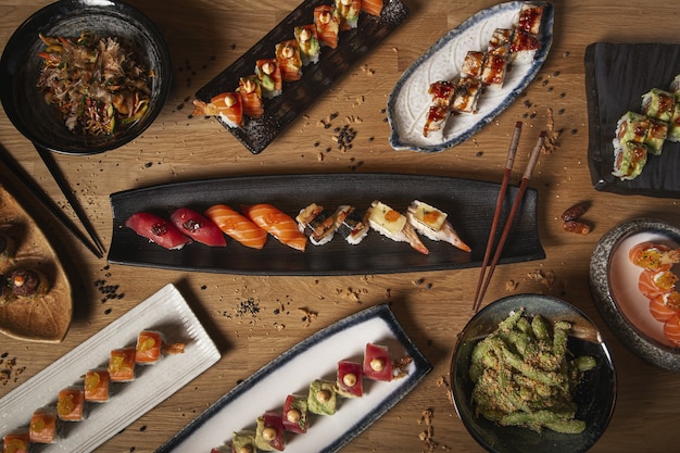 Vista dall'alto di una varietà di sushi, nigiri, sashimi, yakisoba ed edamame su un tavolo di legno del ristorante