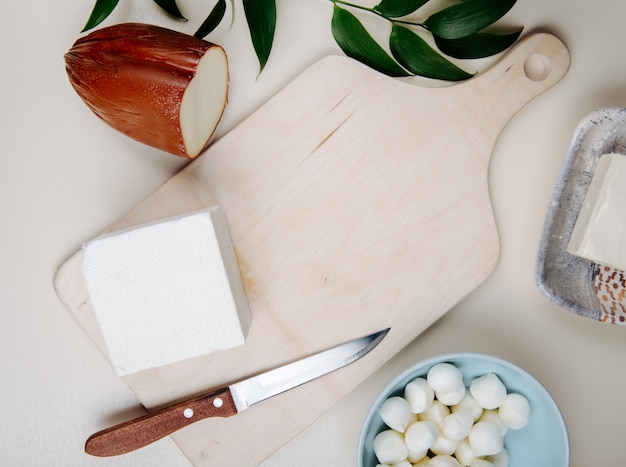 Top view of various cheese on a cutting wooden board with a knife on rustic table