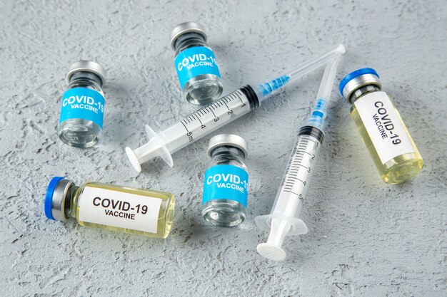 Top view of various covid- vaccines and syringes on gray sand background