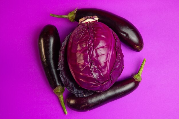 Top view of various fresh vegetables eggplants and red cabbage on purple