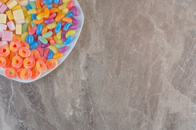 Vista dall'alto di vari tipi di caramelle colorate su piastra bianca su sfondo grigio.