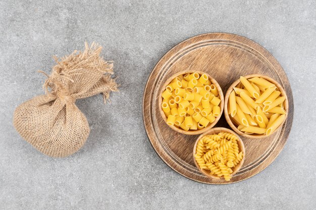 Top view of various kinds of pasta in bowl over wooden board.