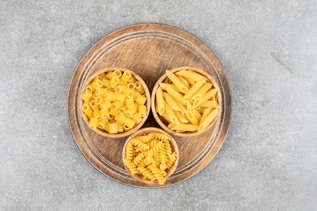 Top view of various kinds of pasta in bowls over wooden board.