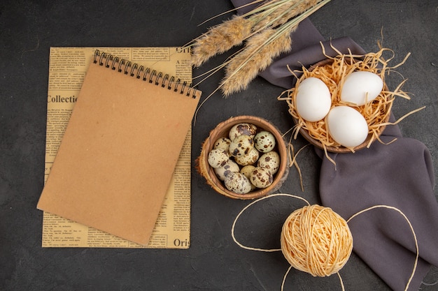 Top view of various organic eggs in a brown pot rope spike black towel spiral notebook on an old newspaper on dark background