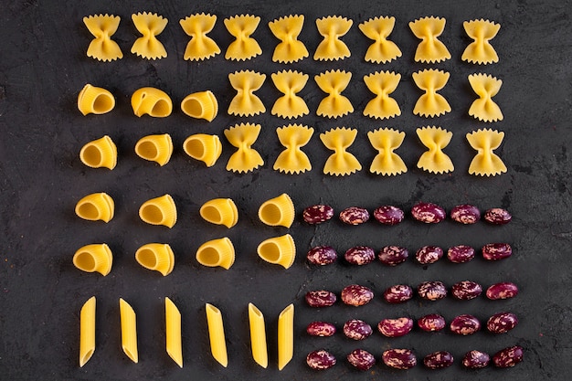 Вид сверху различных сырых макарон с фасолью на черном