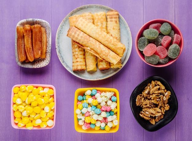 Vista dall'alto di vari dolci per le caramelle di tè marmellate noci e pasticcini su fondo di legno viola