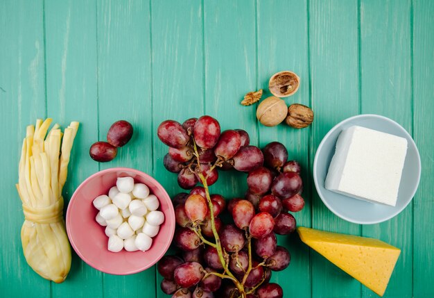 Top view of various types of cheese with fresh grape on green wood with copy space