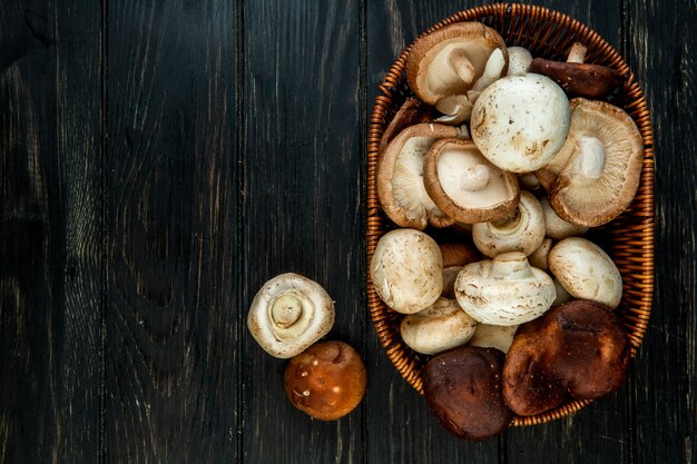 Top view of various types of fresh mushrooms in a wicker basket on dark rustic wood with copy space