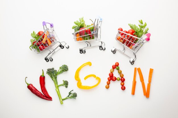 Top view vegan lettering next to small shopping carts