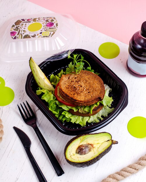 Top view of vegan sandwich with avocado and tomatoes in a delivery box