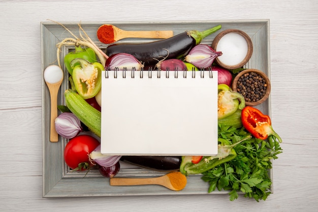 Free photo top view vegetable composition with greens notepad and seasonings on white table