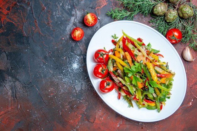 Вид сверху овощной салат на овальной тарелке с помидорами черри на темно-красном столе