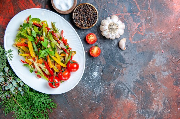 Top view vegetable salad on oval plate cherry tomatoes garlic spices on dark red table free space