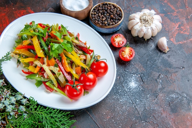 Top view vegetable salad on oval plate cherry tomatoes garlic spices on dark red table