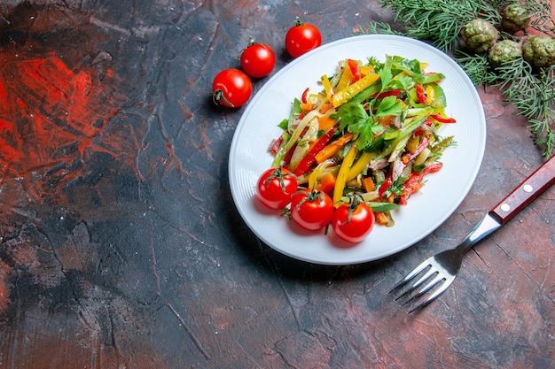 Top view vegetable salad on oval plate fork cherry tomatoes on dark red table