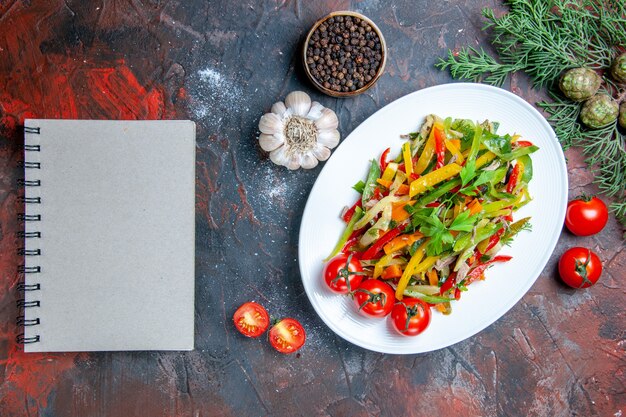 楕円形のプレートのメモ帳にトップビュー野菜サラダ濃い赤のテーブルに黒胡椒にんにくのメモ帳