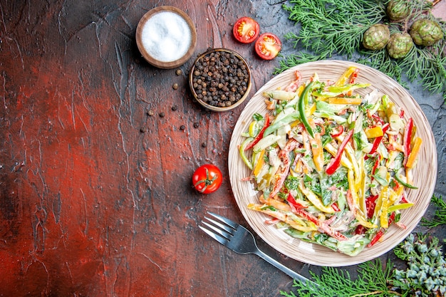 Top view vegetable salad on plate fork salt and black pepper tamatoes on dark red table with copy space