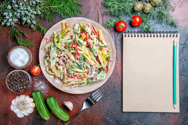 平面図野菜サラダプレートフォークトマト松枝きゅうりニンニク鉛筆メモ帳濃い赤のテーブル