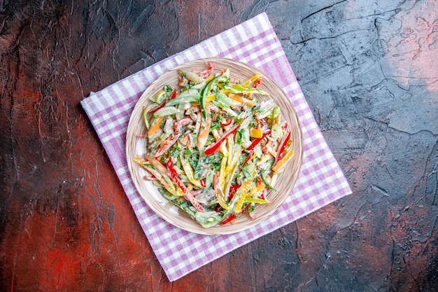 Top view vegetable salad on plate on tablecloth on dark red table copy place