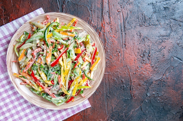 Top view vegetable salad on plate on tablecloth on dark red table free space