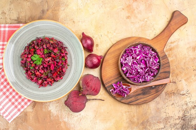 Top view vegetable salad with green leaves with beetroots red onions and bowl of chopped cabbage on a wooden background with space for text