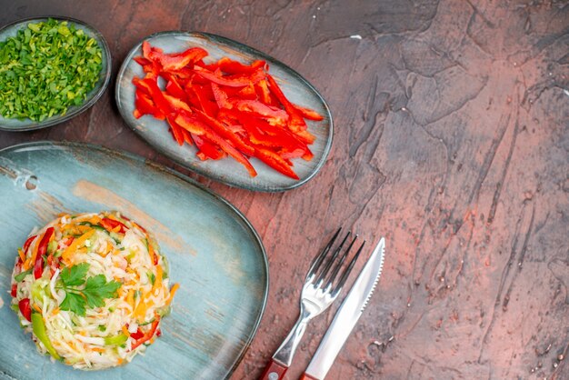 Top view vegetable salad with greens and sliced bell-peppers on dark table