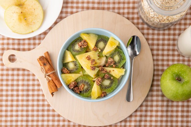 Top view vegetable salad with kiwi pineapple and cinnamon on a board with a spoon