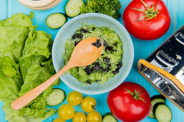 Top view of vegetable salad with lettuce cucumber tomato coriander and grater with wooden spoon on blue surface