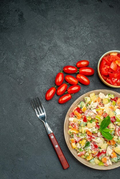 Top view of vegetable salad with tomatoes and fork on dark grey background