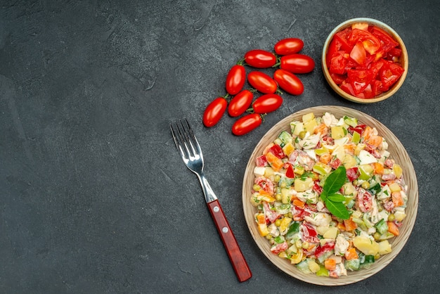 Top view of vegetable salad with tomatoes and fork on dark grey background