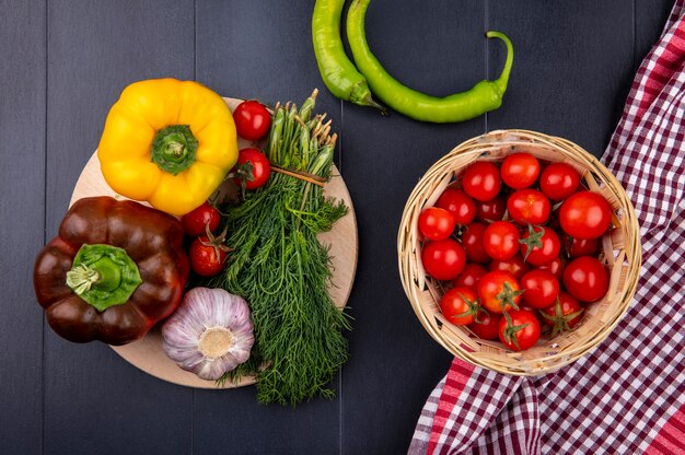 검은 표면에 커팅 보드에 딜의 고추 토마토 마늘 무리와 격자 무늬 천으로 토마토 바구니로 야채의 상위 뷰